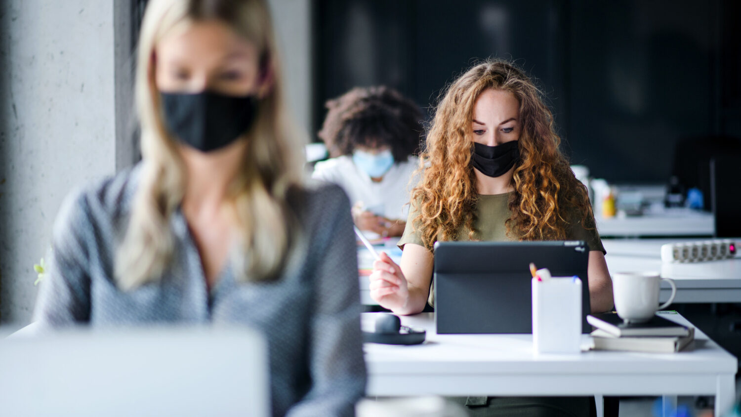Young people with face masks back at work or school in office after lockdown.